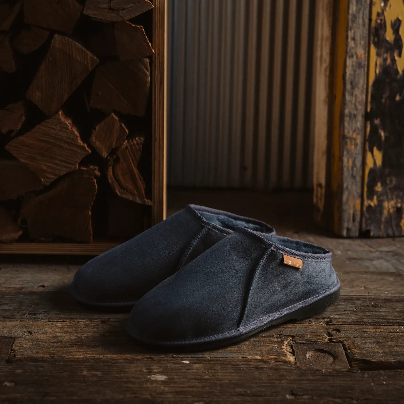 Pair of blue suede navy ugg slip-on mewels on a wooden floor with a rustic background