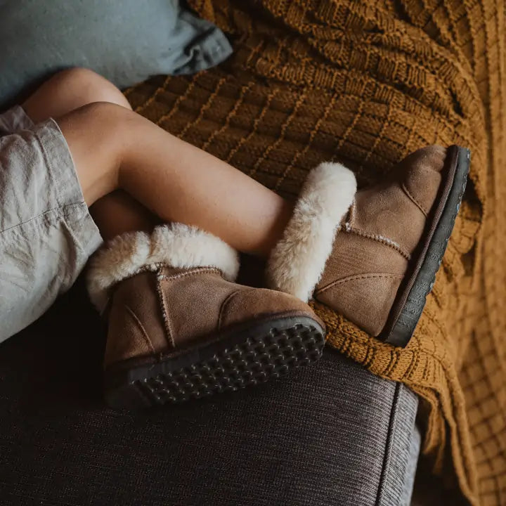 Close up on a kid wearing Jassi toddler ugg boots in suede tan with a fluffy wool turn. #color_tan