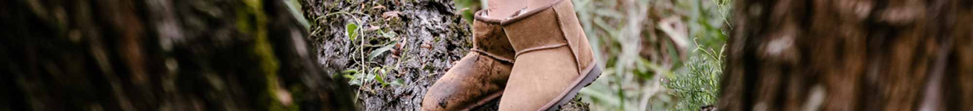 Close up of a kid wearing tan suede ugg boots standing on a tree.