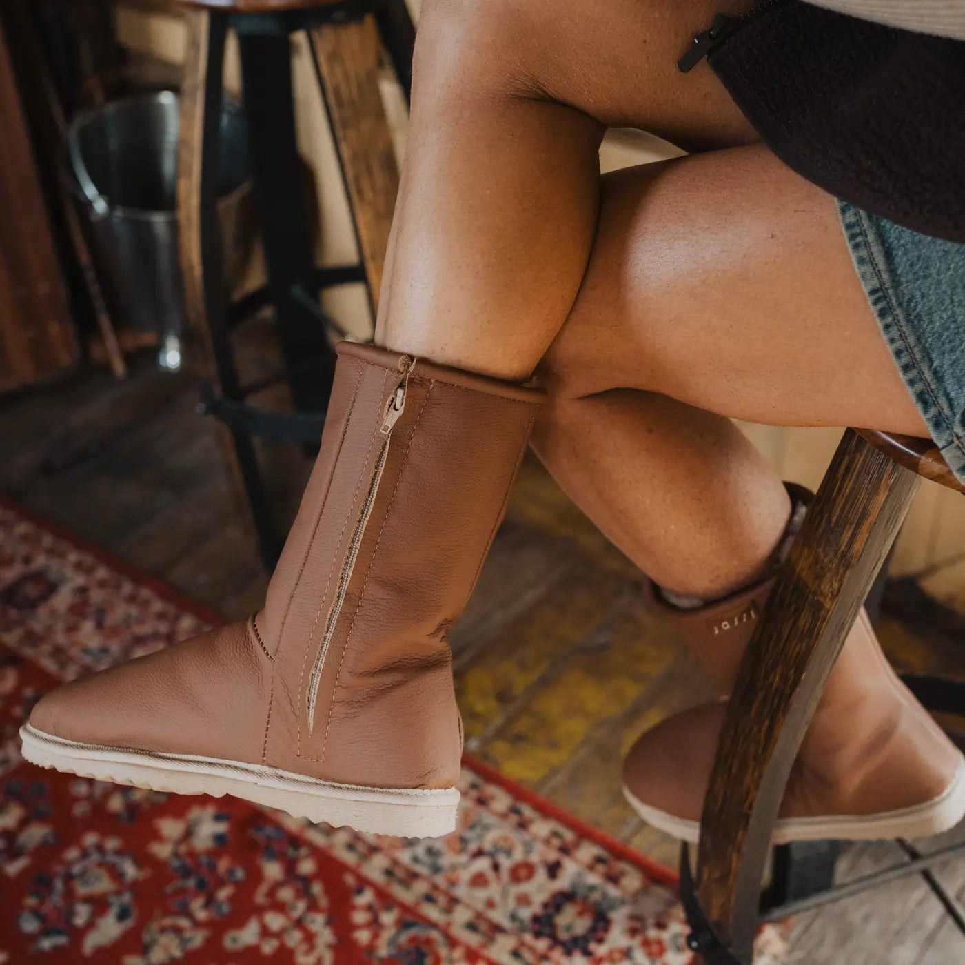 Woman wearing  mid tan leather Jassi Ugg boots sitting on a stool indoors.