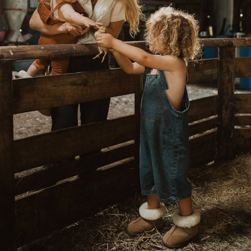 Kid holding a little chicken while wearing baby ugg boots in suede tan with fluffy wool turn.