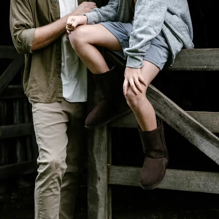 Kid sitting on a fence with his dad wearing Jassi Suede boots in Chocolate color. #color_chocolate