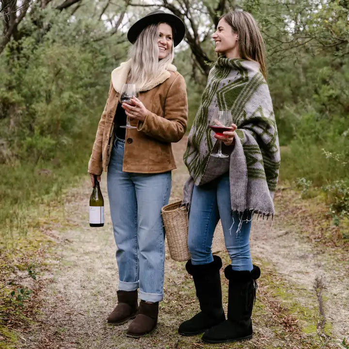 Two friends having a walk in the forest while enjoying a wine and wearing Jassi Long Lace-Up Boots in suede black #color_black