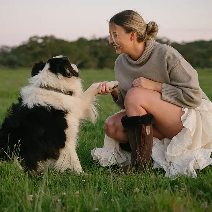 Woman playing with a dog wearing Jassi long lace-up UGG boots on suede chocolate. #color_chocolate