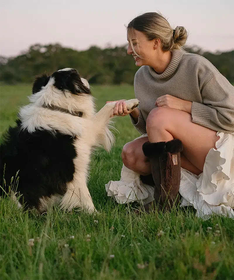 Woman playing with a dog on a field while wearing long lace-up ugg boots in suede chocolate color.