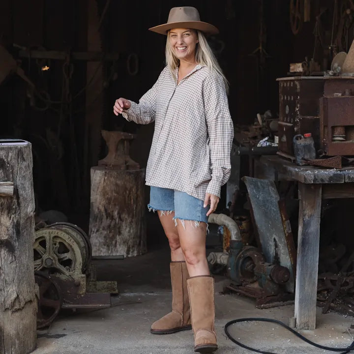 Woman on a farm shed wearing Jassi long ugg boots in suede tan. #color_tan