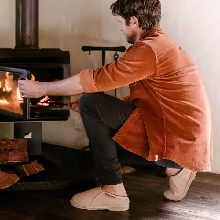 Man throwing wood in a fireplace while wearing cosy Jassi mewels in suede sand.