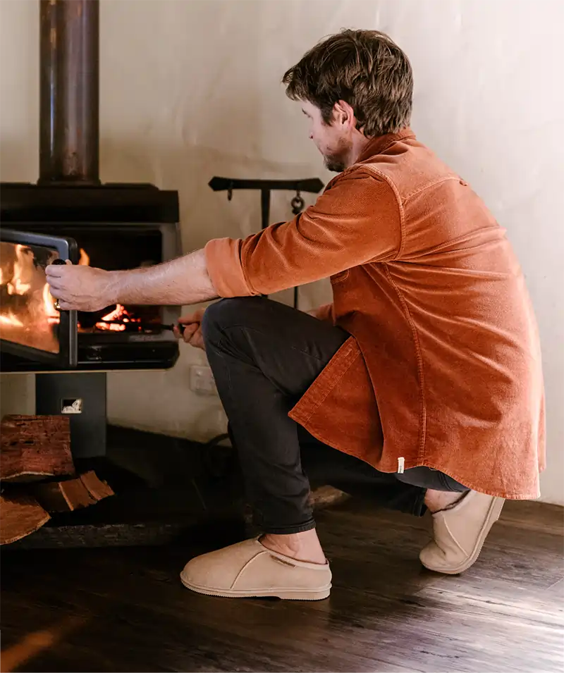 Man stocking the fire while wearing Jassi ugg mewels in suede sand.