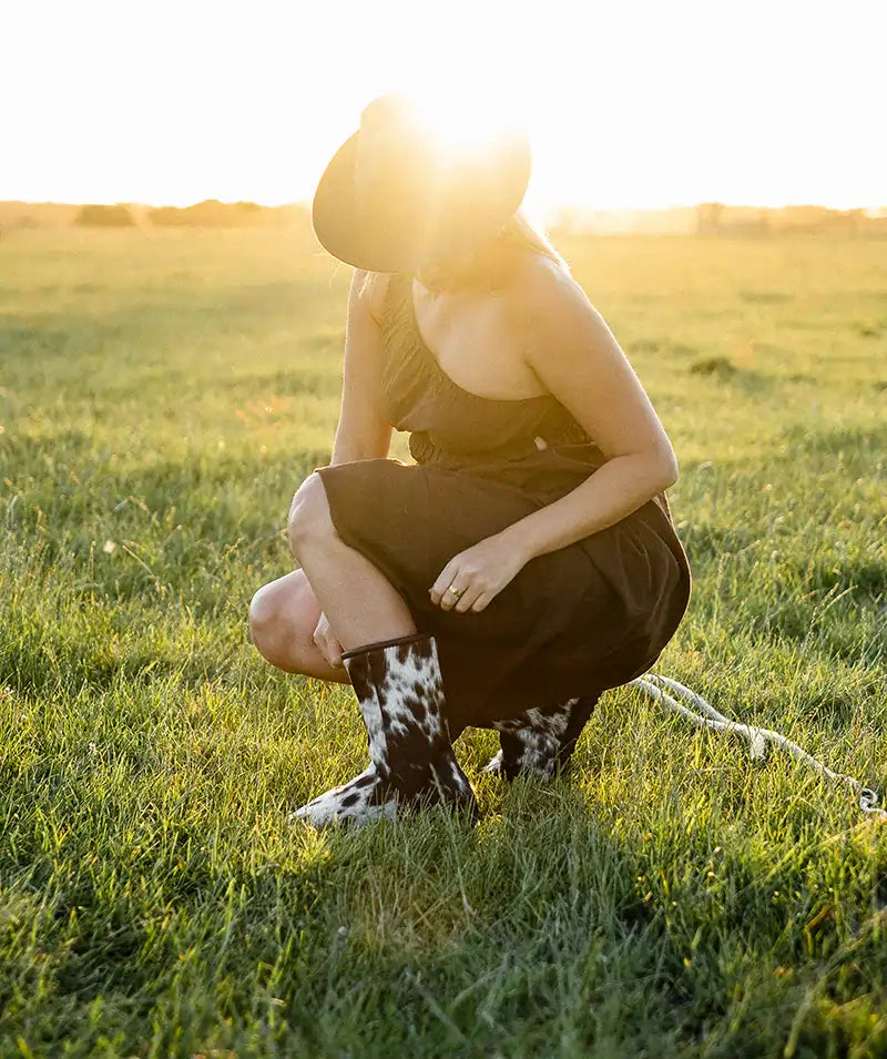 Woman on a green field adjusting her Jassi mid ugg boots made with cowhide.