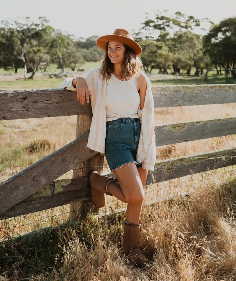 Woman leaning on a fence wearing Jassi mid ugg boots in suede tan.