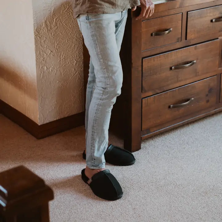 Close up of a man indoors wearing Jassi ugg leather scuffs in black.#color_leather black