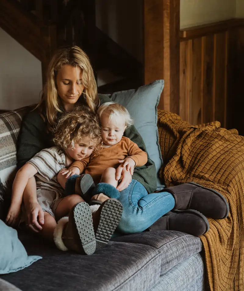 Woman holding her kids wearing Jassi short ugg boots in suede chocolate color.