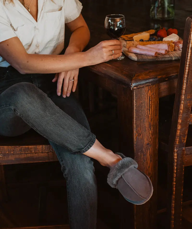 Woman enjoying a wine indoors while wearing comfy ugg scuffs in suede grey color.