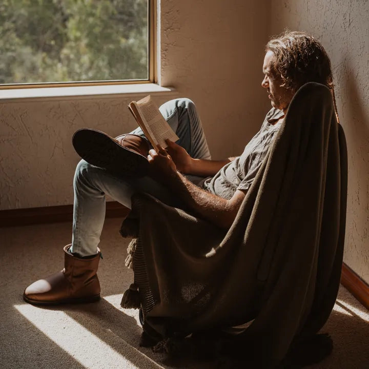 Man reading while wearing Jassi Short ugg boots on genuine leather in tan color. #color_leather tan