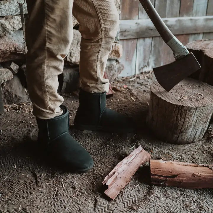 Man chopping wood wearing Jassi short UGG boots on black suede color, close up. #color_black