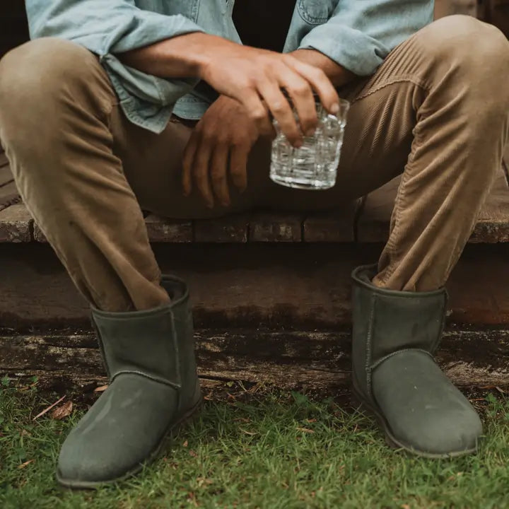 Man wearing Jassi short ugg boots in suede finish and olive color while sitting ourside having a drink.. #color_olive