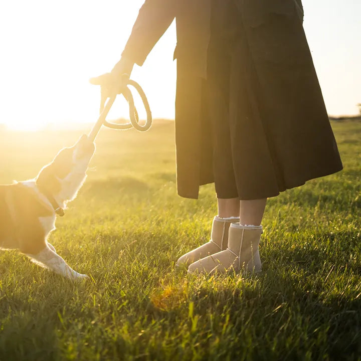 Woman playing with dog while wearing Jassi Short UGG Boots in suede sand color. #color_sand