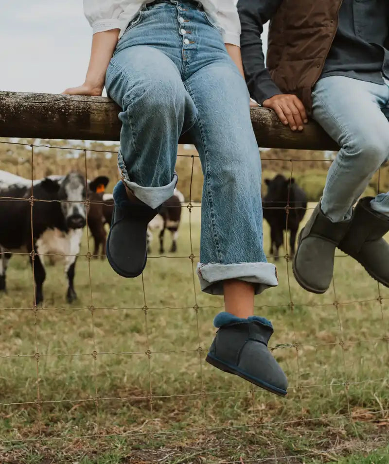 Woman sitting on a fence while wearing Jassi ugg slippers in navy.