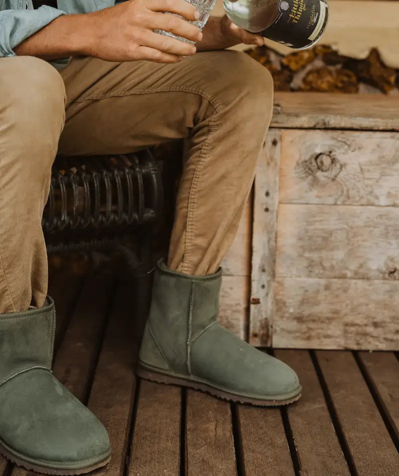 Man puring a drink while wearing short suede olive ugg boots.