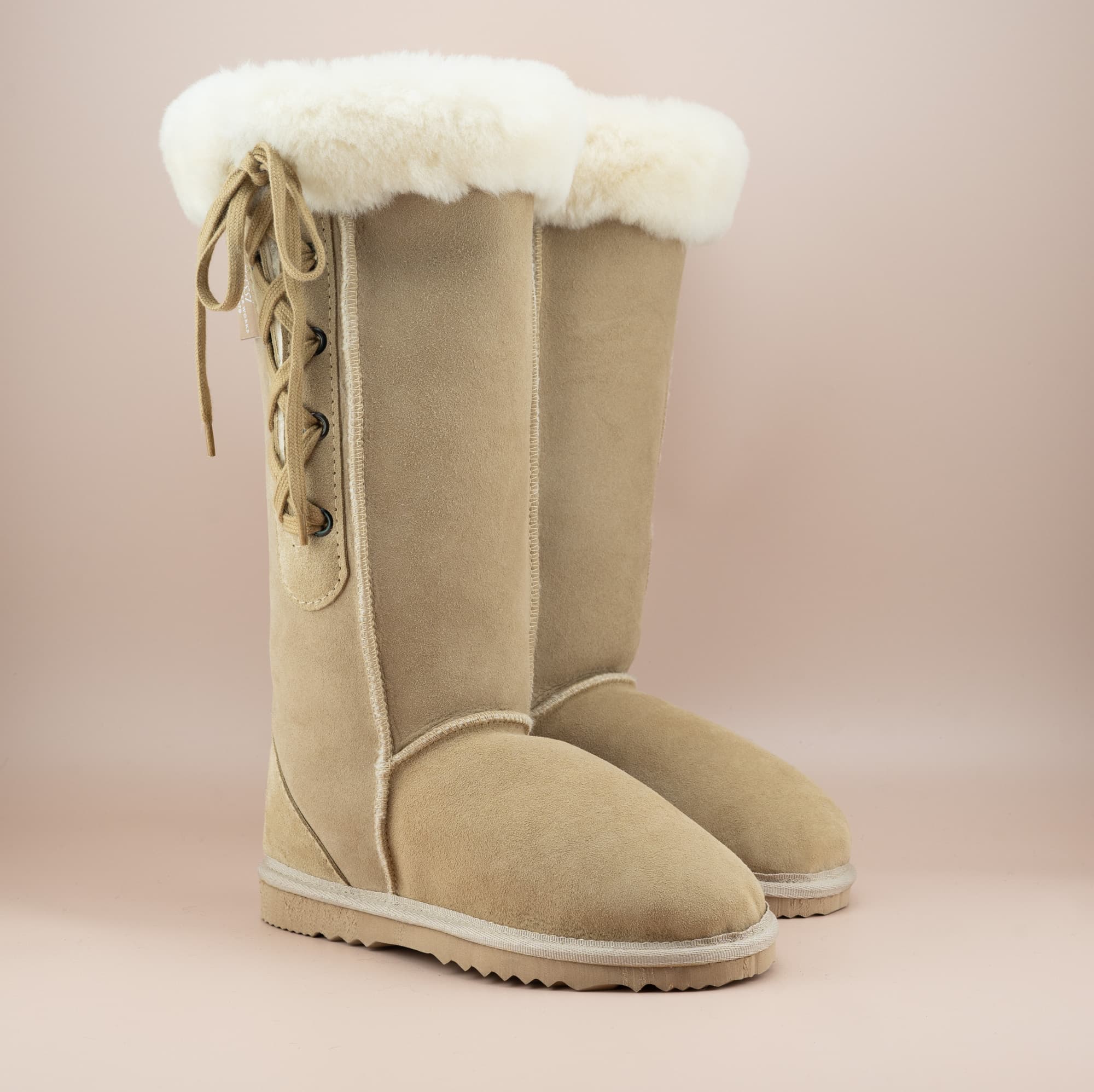 Men's long lace-up ugg boot in color sand and soft suede finish with signature wool turn, front side view. #color_sand