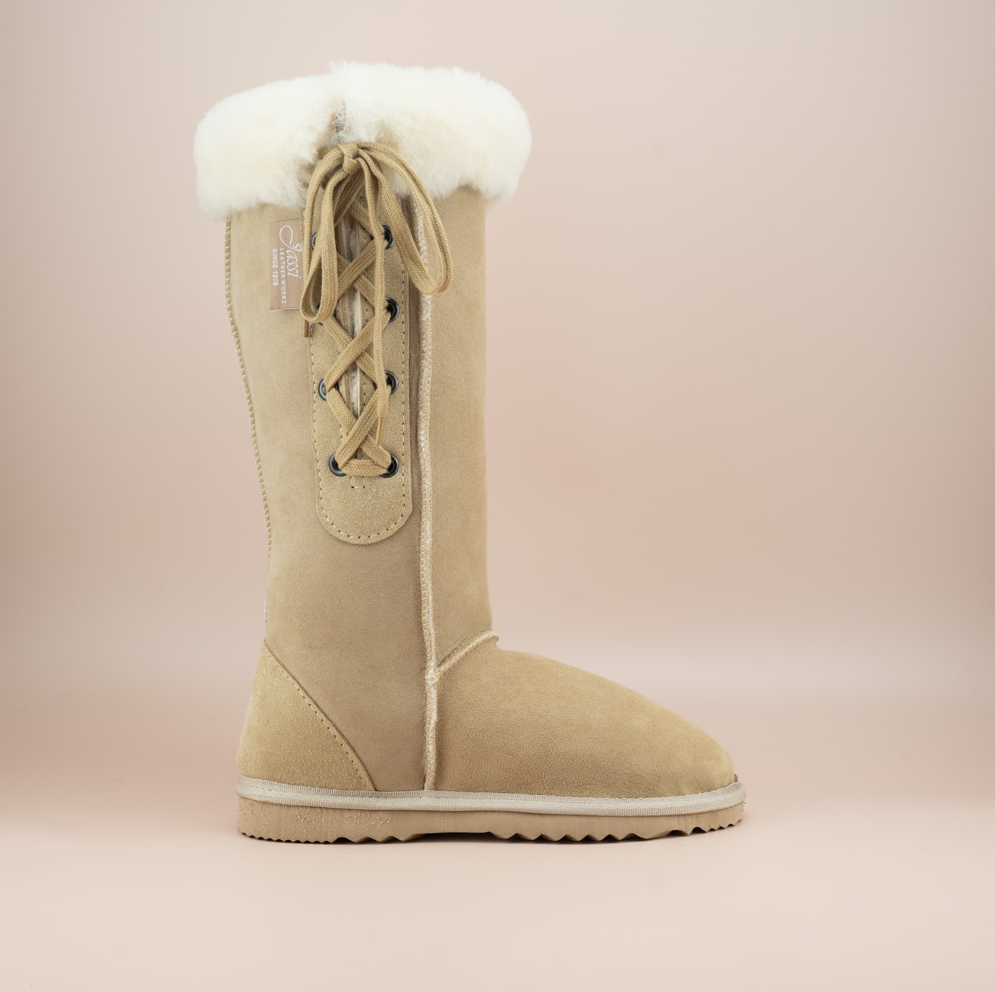 Men's long lace-up ugg boot in color sand and soft suede finish with signature wool turn, side view. #color_sand