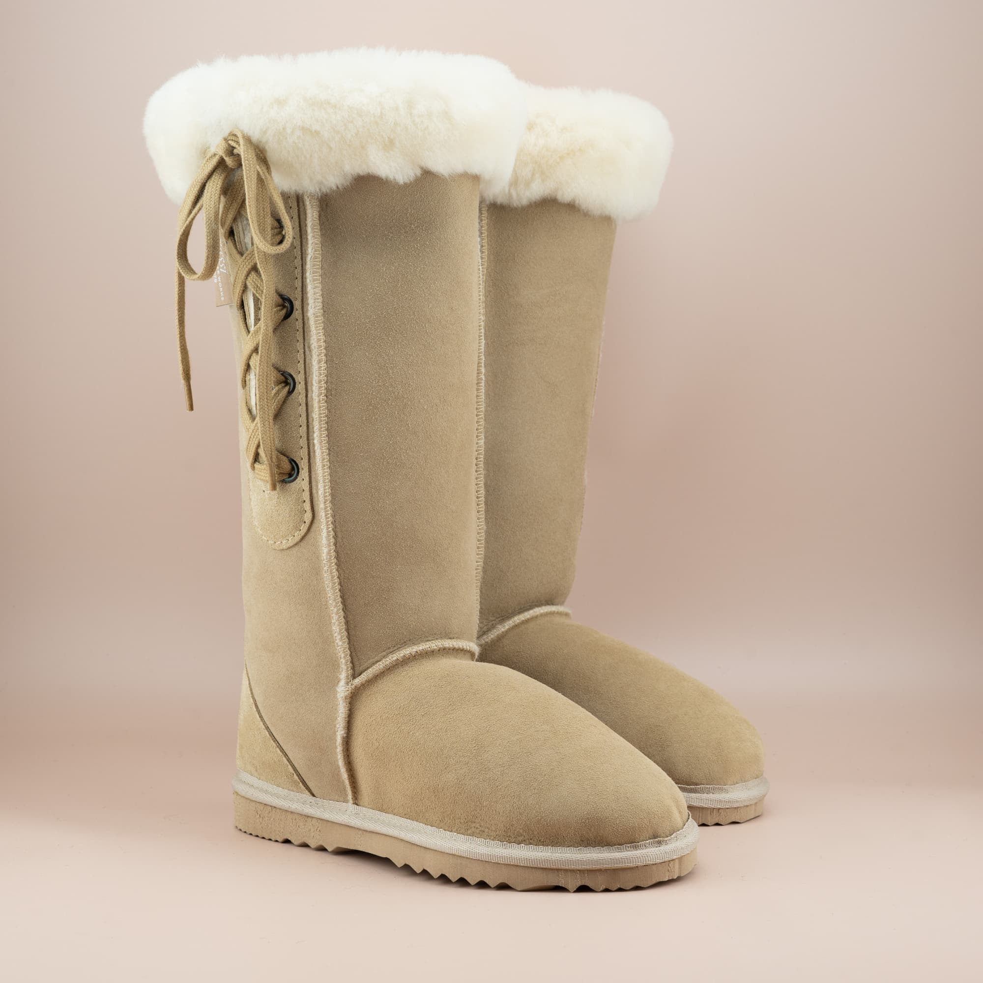 Women's classic long lace-up ugg boot with a cosy wool turn in suede sand color, front side view. #color_sand